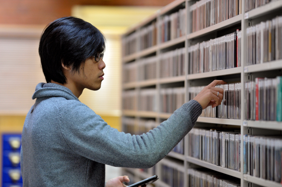 An Asian male student, looking in a library.